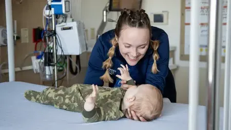 Nursing student caring for an infant on a examination table.